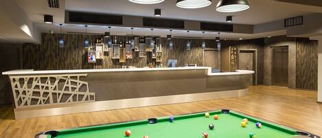 A pool table with balls, a bar area with bottles, and pendant lighting.