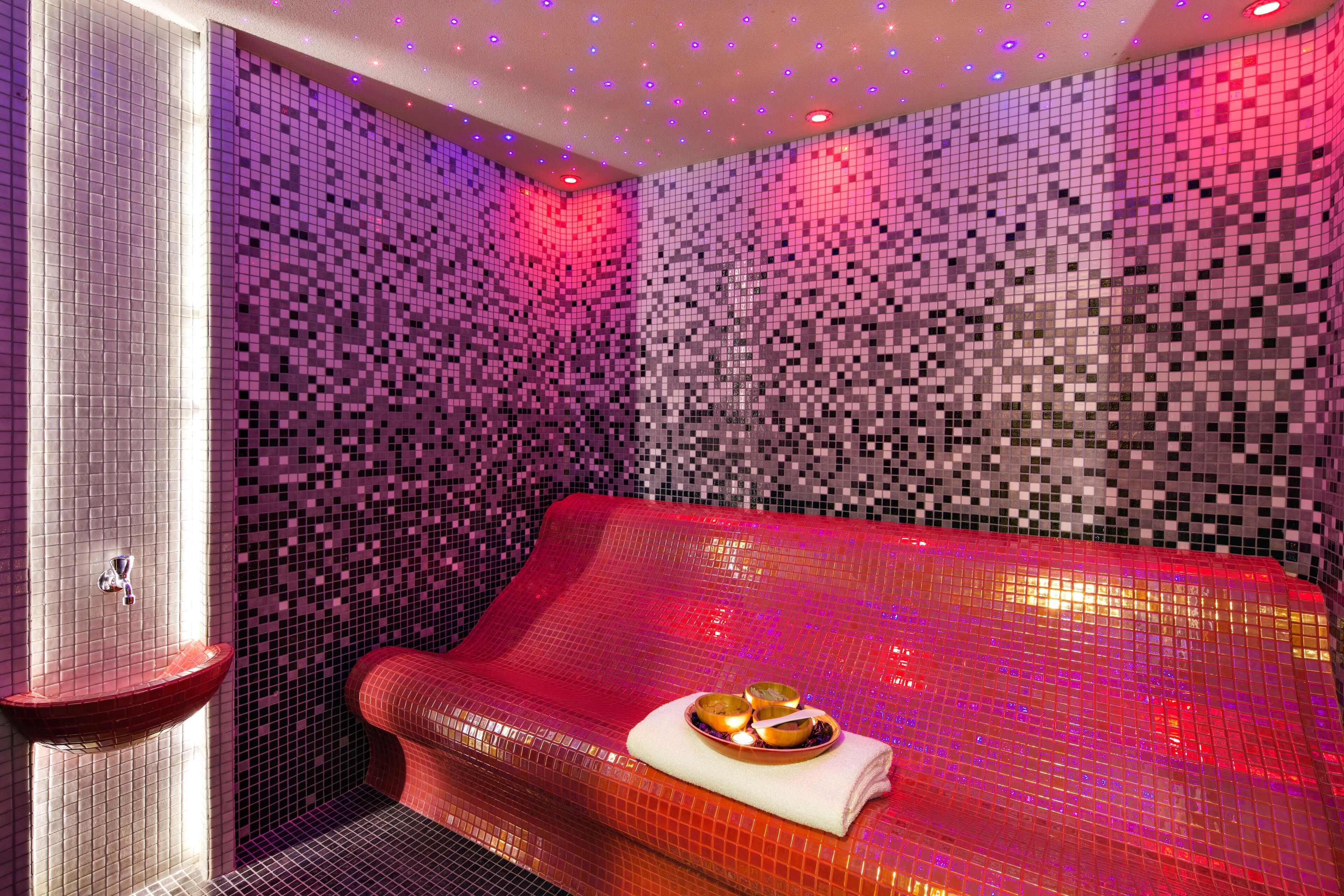A modern spa room with a mosaic tiled wall, a red bench, and a small sink.