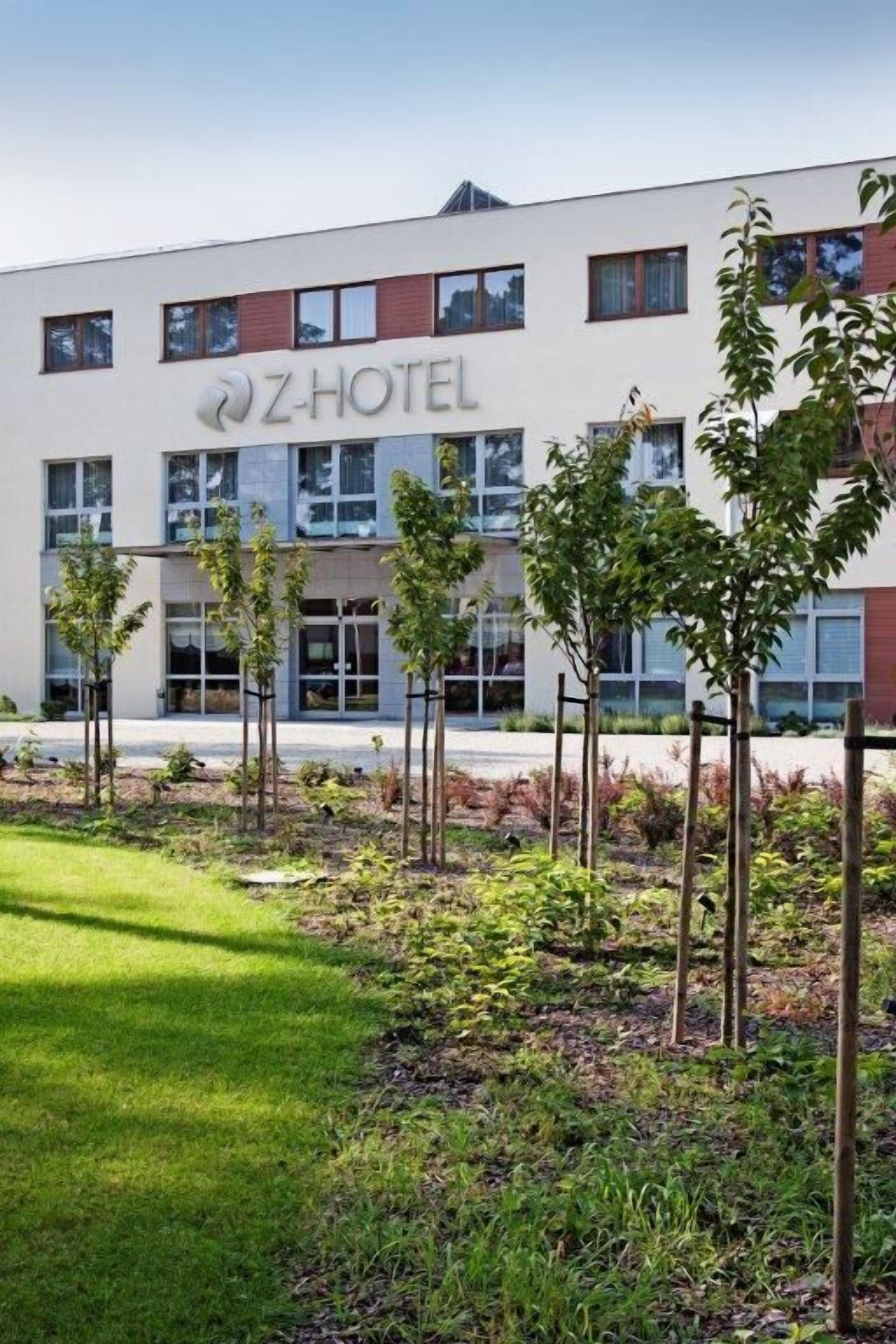 Un edificio moderno del Z-Hotel, con fachada plana, múltiples ventanas y un césped bien cuidado con árboles jóvenes.