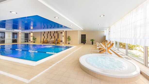 An indoor swimming pool with a hot tub, wooden loungers, and a view through large windows. - Z-Hotel Business & Spa (Otwock)
