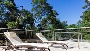 Two sun loungers with wheels on a tiled patio with a glass railing, surrounded by trees. - Z-Hotel Business & Spa (Otwock)