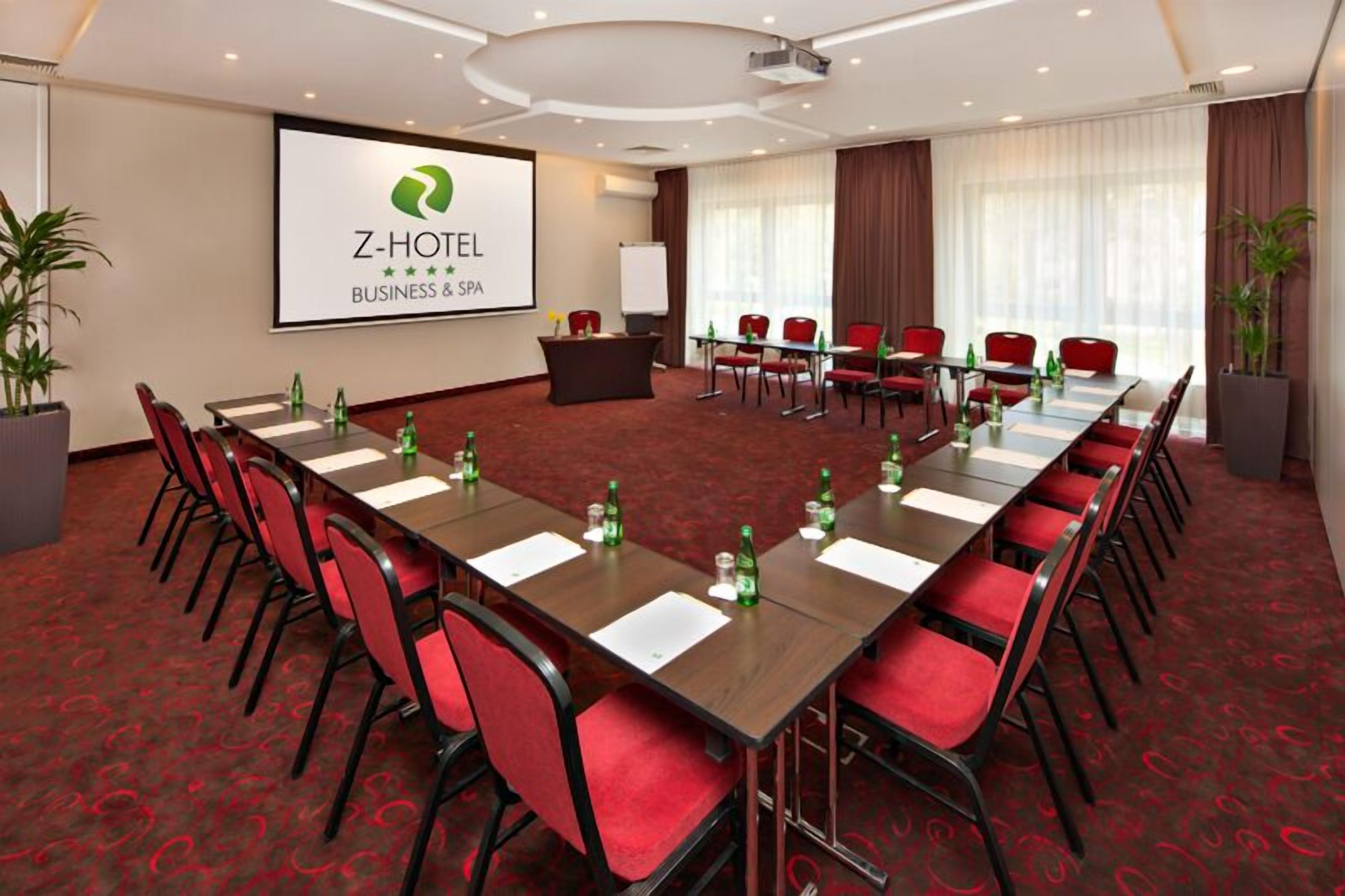 Una sala de conferencias de Z-Hotel para negocios, con una pantalla grande, sillas rojas y piso alfombrado.