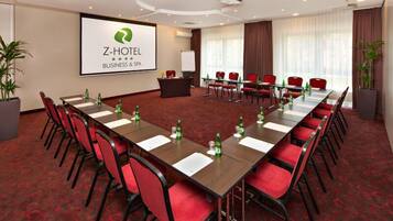Una sala de conferencias de Z-Hotel para negocios, con una pantalla grande, sillas rojas y piso alfombrado.