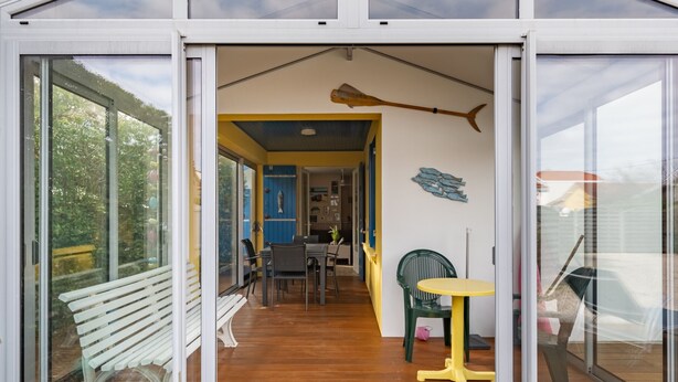 A modern house with a large glass door leading to a dining area with a bench and a table. - Cozy Villa Steps from Beach in Biscarrosse - WiFi, Terrace, Garden, Sleeps 6 (Biscarrosse Plage)