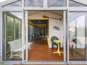 A modern house with a large glass door leading to a dining area with a bench and a table. - Cozy Villa Steps from Beach in Biscarrosse - WiFi, Terrace, Garden, Sleeps 6 (Biscarrosse Plage)