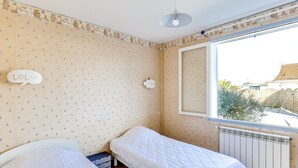 A room with two beds, a radiator, a window with a view of the outside, and a wall with a bear pattern. - Cozy Villa Steps from Beach in Biscarrosse - WiFi, Terrace, Garden, Sleeps 6 (Biscarrosse Plage)