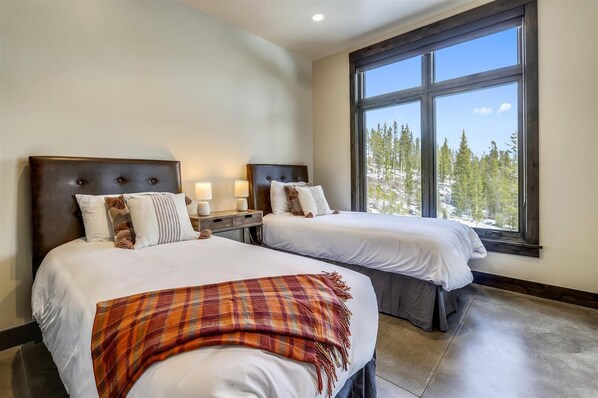 A hotel room with two beds, a large window with a view of trees, and a nightstand with lamps.