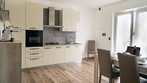 A modern kitchen with white cabinets, a built-in oven, and a dining area with a table and chairs. - House stefi 2 M0230450730 (Malcesine)