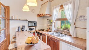 Een keuken met een fornuis, magnetron, spoelbak en een schaal fruit op het aanrecht.