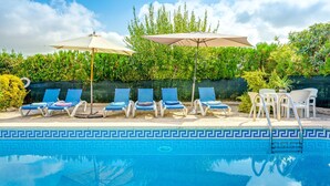 Zwembad met blauwe tegels, omringd door ligbedden en parasols.