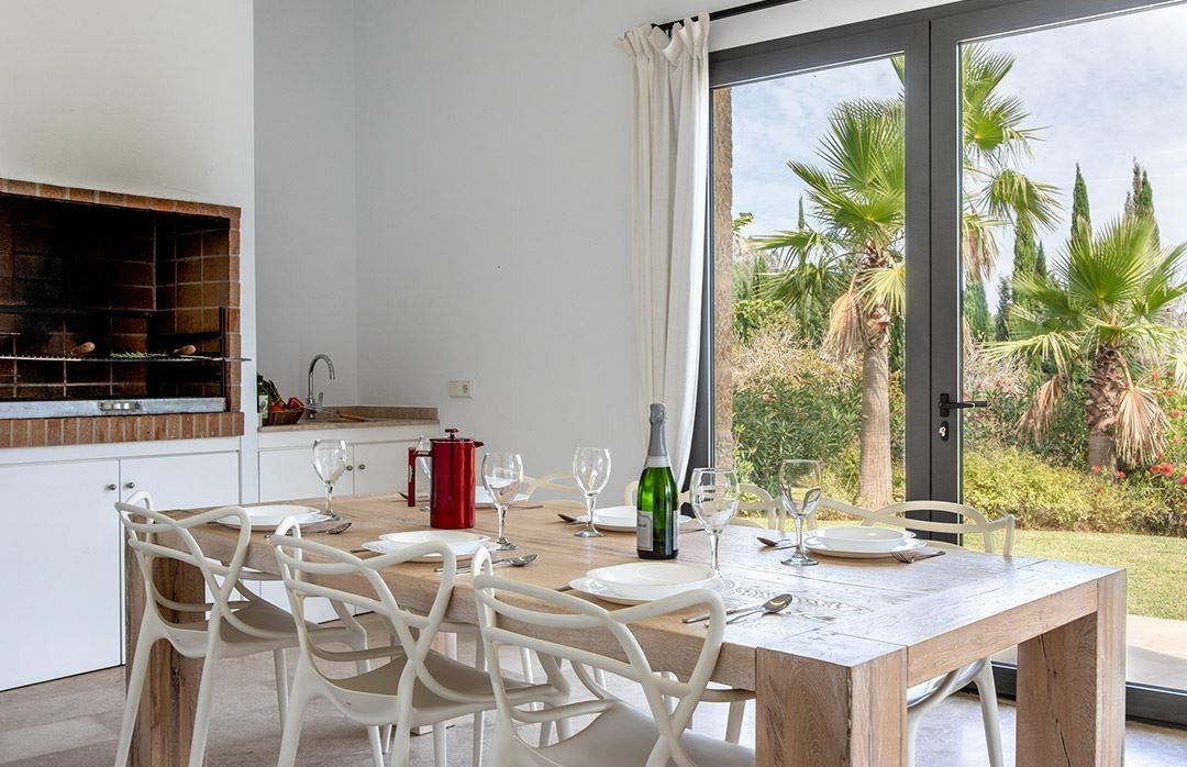 A dining area with a wooden table, white chairs, and a view of a garden through a glass door.
