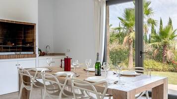 A dining area with a wooden table, white chairs, and a view of a garden through a glass door.