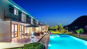 Une maison moderne dotée d’une piscine, d’un espace salon extérieur et offrant une vue sur une colline.