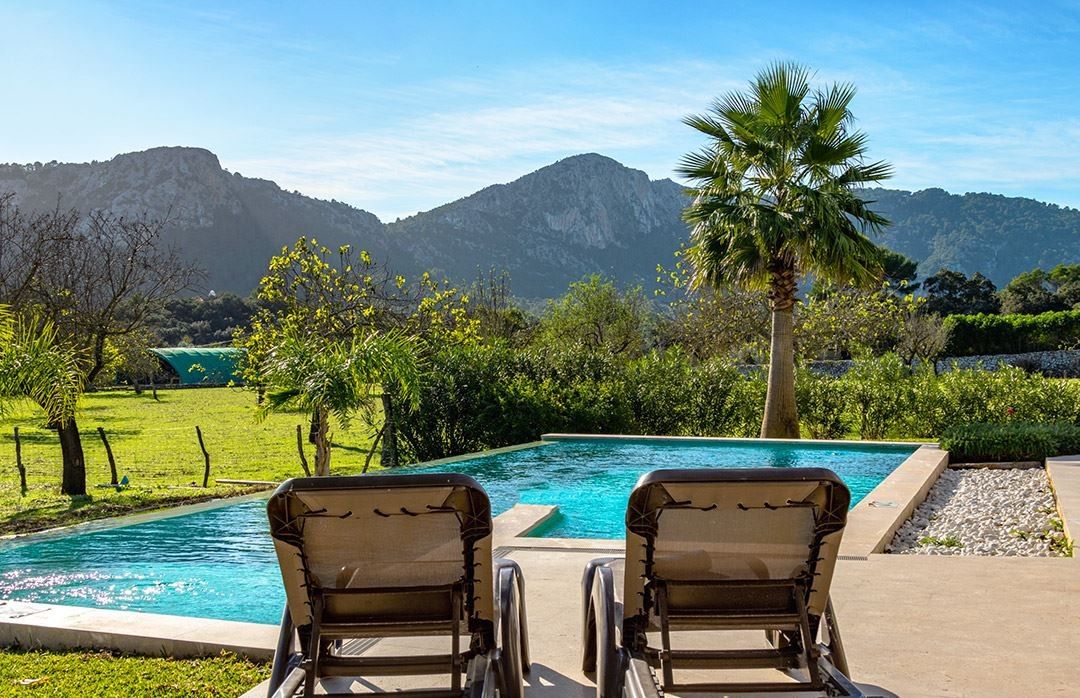 A pool with two lounge chairs facing a mountain backdrop.
