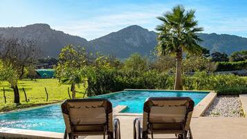 A pool with two lounge chairs facing a mountain backdrop.