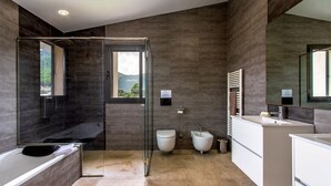 Une salle de bain moderne dotée d’une douche à parois de verre, d’une baignoire, de toilettes, d’un bidet et d’un meuble-lavabo avec un miroir.