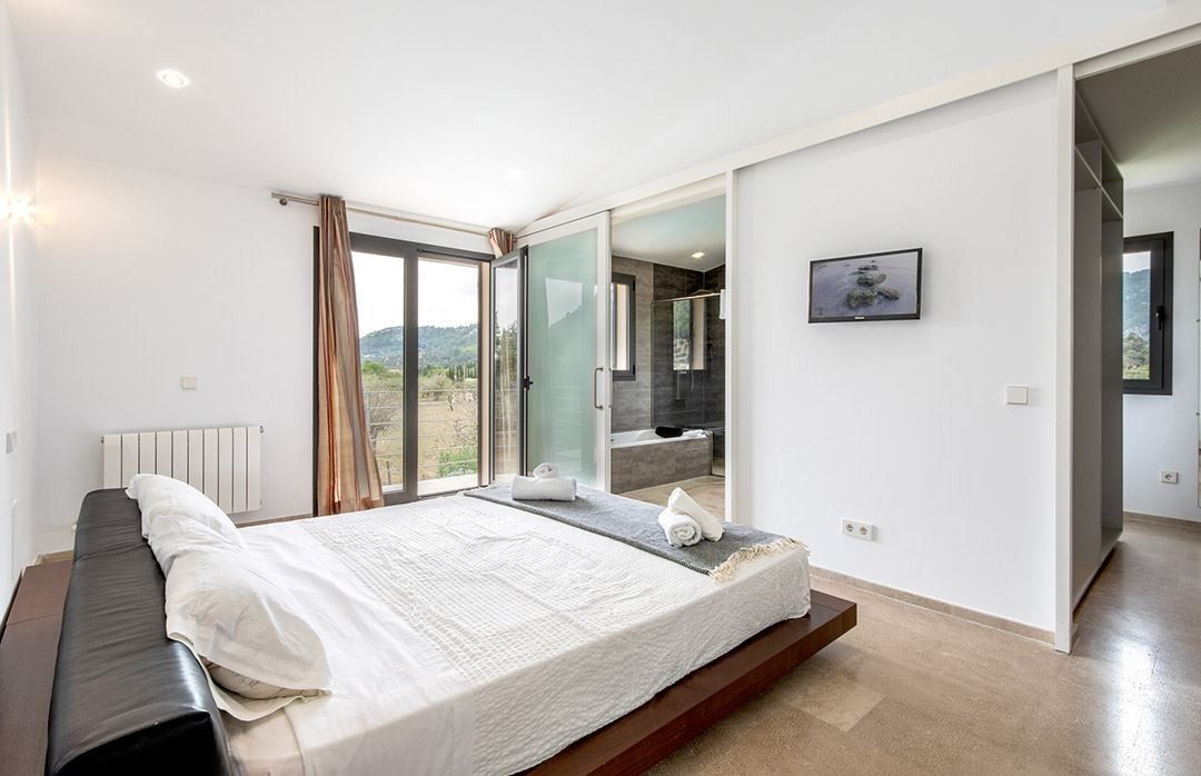 Een moderne slaapkamer met een groot bed, een schuifglasdeur naar een balkon en uitzicht op de natuur.