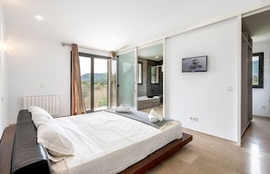 A modern bedroom with a large bed, a sliding glass door to a balcony, and a view of the outdoors.