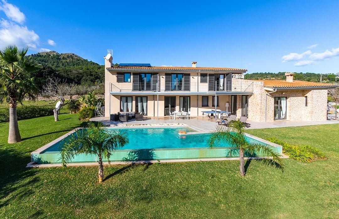 Een tweelaags huis met een zwembad, terras en uitzicht op een berg.