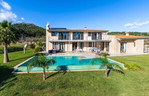 A two-story house with a swimming pool, outdoor seating, and a view of a mountain.