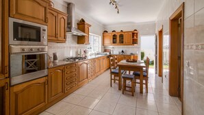 A kitchen with wooden cabinets, a built-in oven, a stove, and a dining area with a table and chairs. - Holiday Home "Villa Do Lago" with Sea View, Balcony, Garden & Pool (Albufeira)