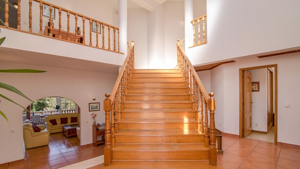 A staircase with wooden railings leading to an upper level, a living area with a sofa and a coffee table, and a door on the right. - Holiday Home "Villa Do Lago" with Sea View, Balcony, Garden & Pool (Albufeira)