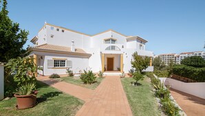 A two-story white building with a tiled roof, a central entrance, and a paved pathway leading to the entrance. - Holiday Home "Villa Do Lago" with Sea View, Balcony, Garden & Pool (Albufeira)