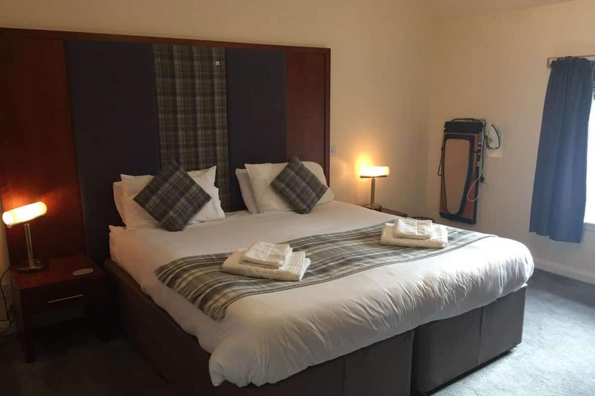 A hotel room with a large bed, two bedside lamps, a mirror, and a window with curtains.