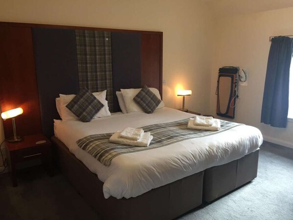 A hotel room with a large bed, two bedside lamps, a mirror, and a window with curtains.