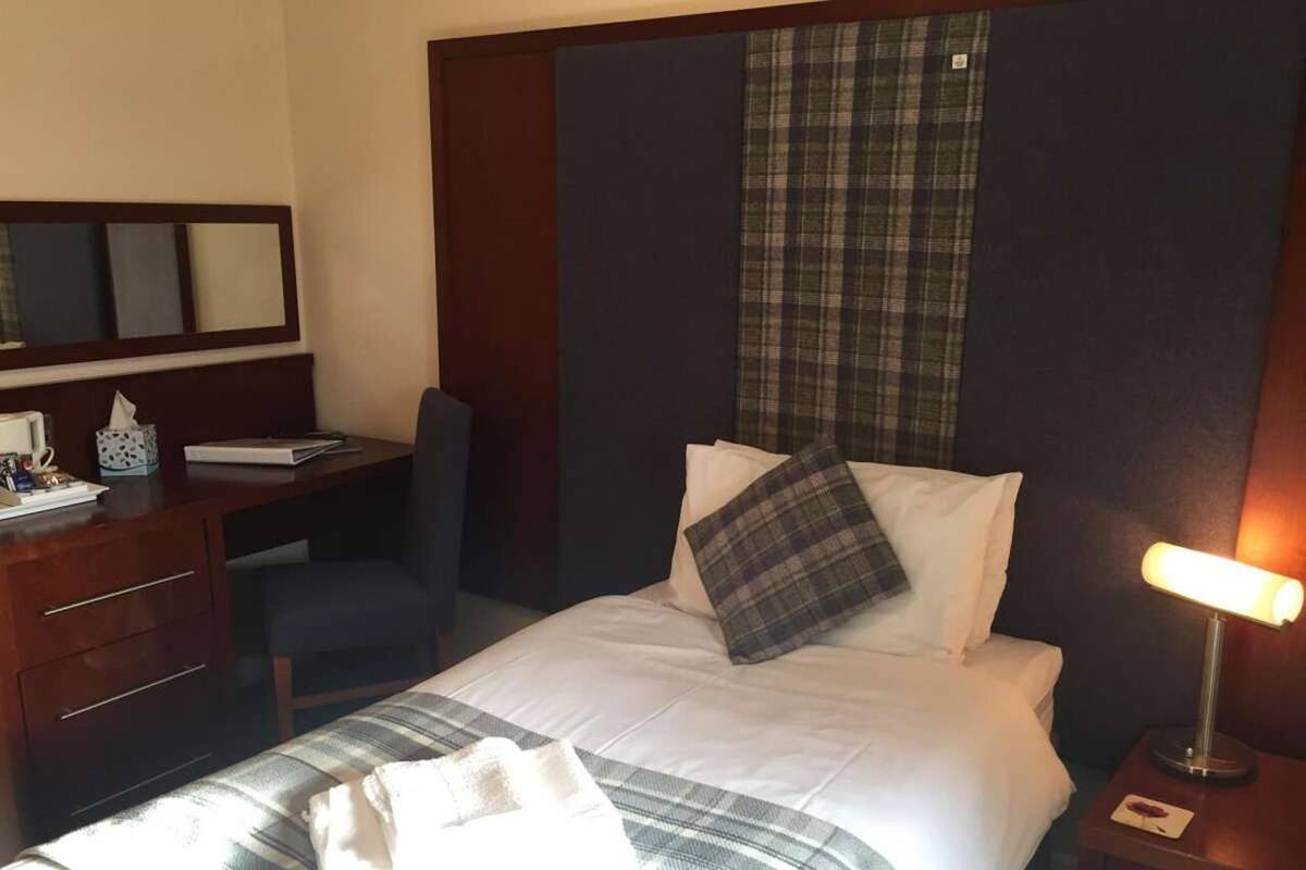 A hotel room with a bed, a desk, a chair, a lamp, and a mirror.