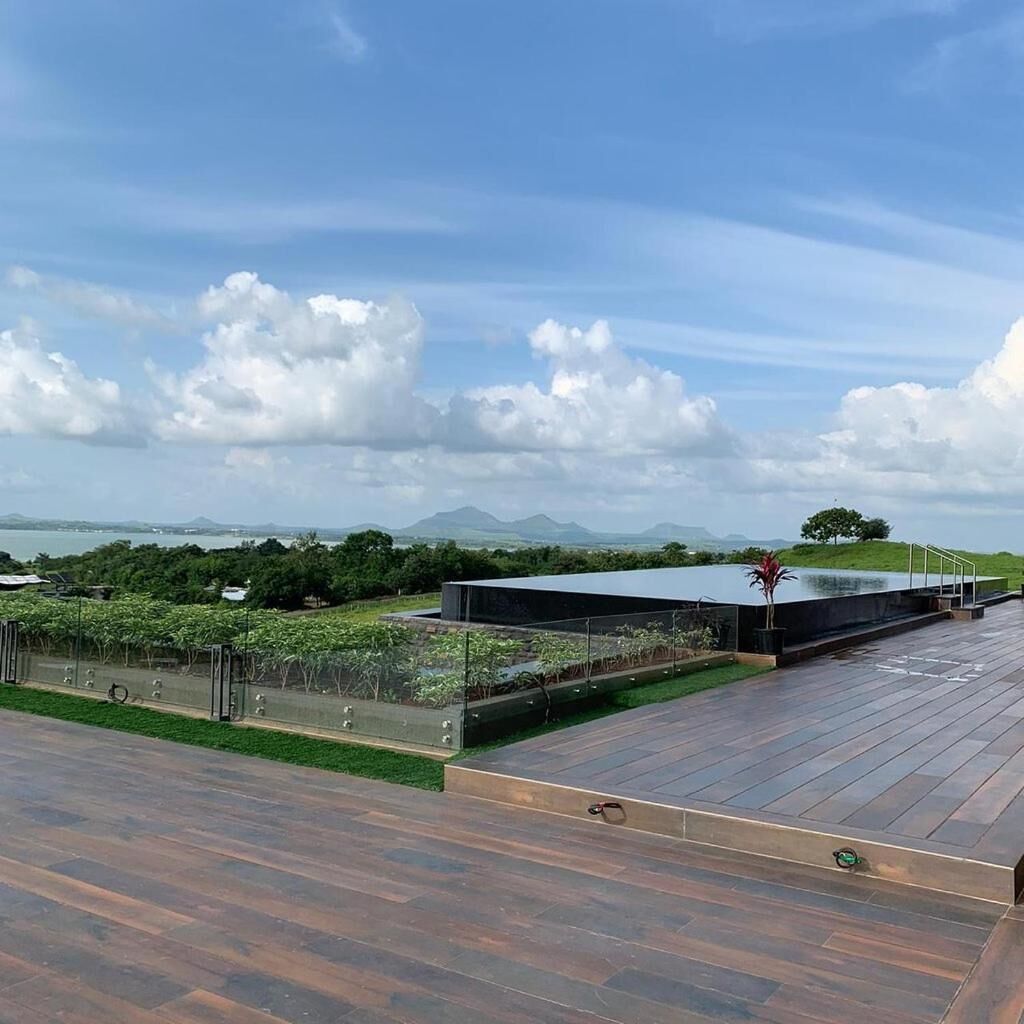Terraza en la azotea con vista a un lago y montañas, rodeada de vegetación y una estructura arquitectónica moderna.
