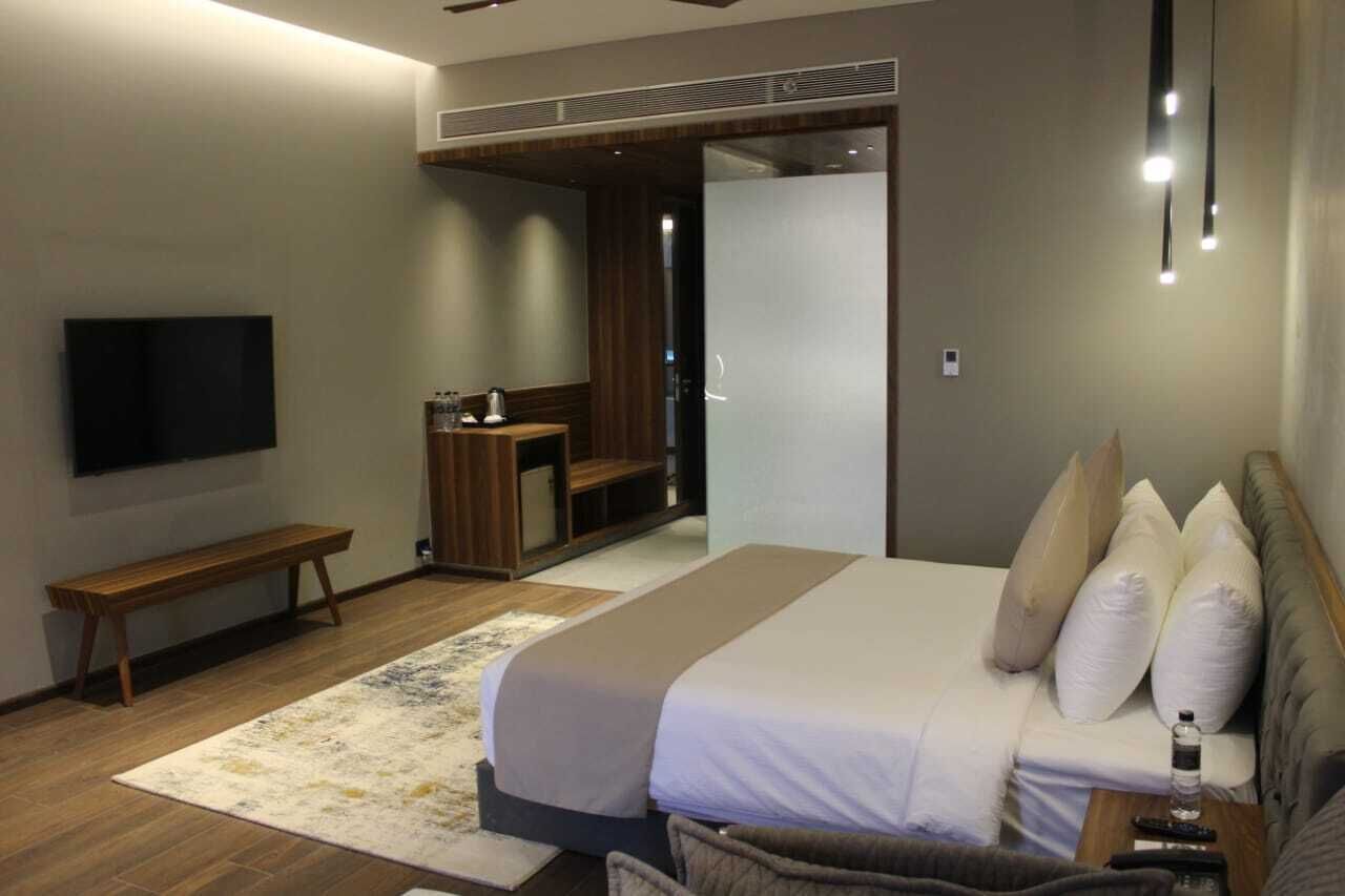 A modern hotel room with a large bed, a bench, a TV, and a desk with a chair.