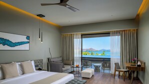 Habitación de hotel con una cama grande, un sofá, un escritorio con una silla y un balcón con vista al lago.