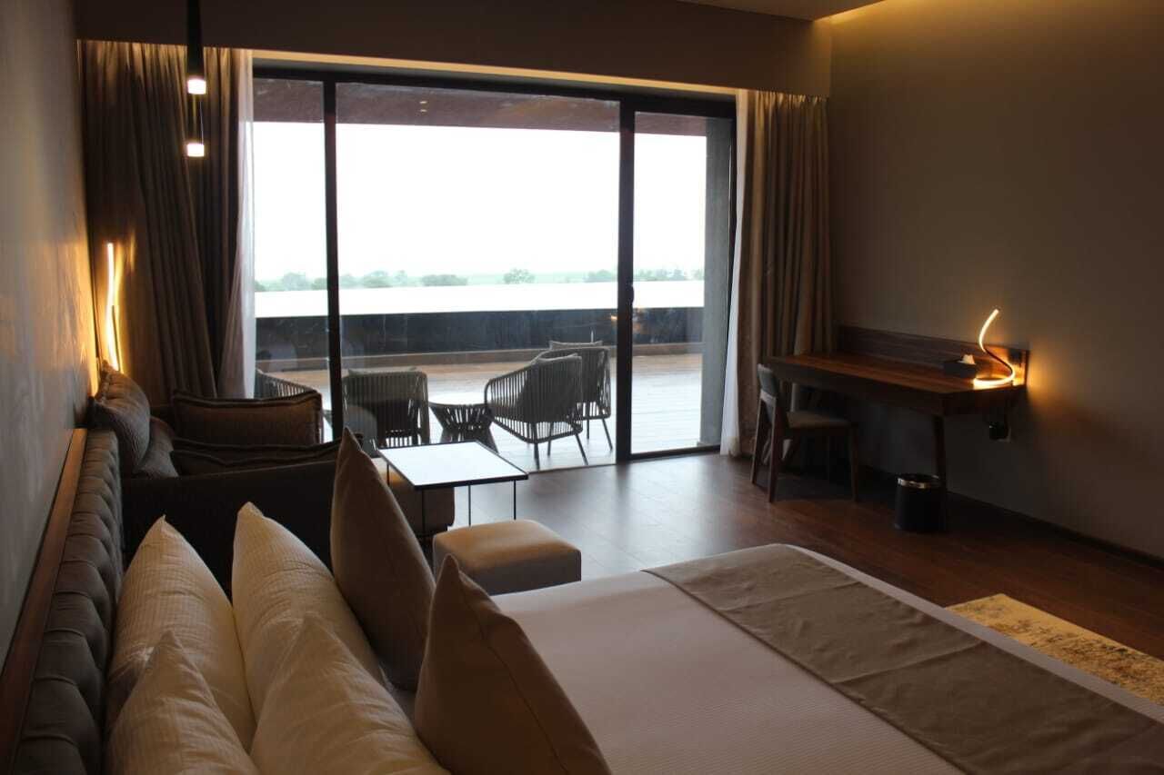 Una habitación de hotel moderna con una cama grande, una zona de estar con sofá y sillones, un escritorio pequeño y vistas al exterior a través de una puerta corredera.