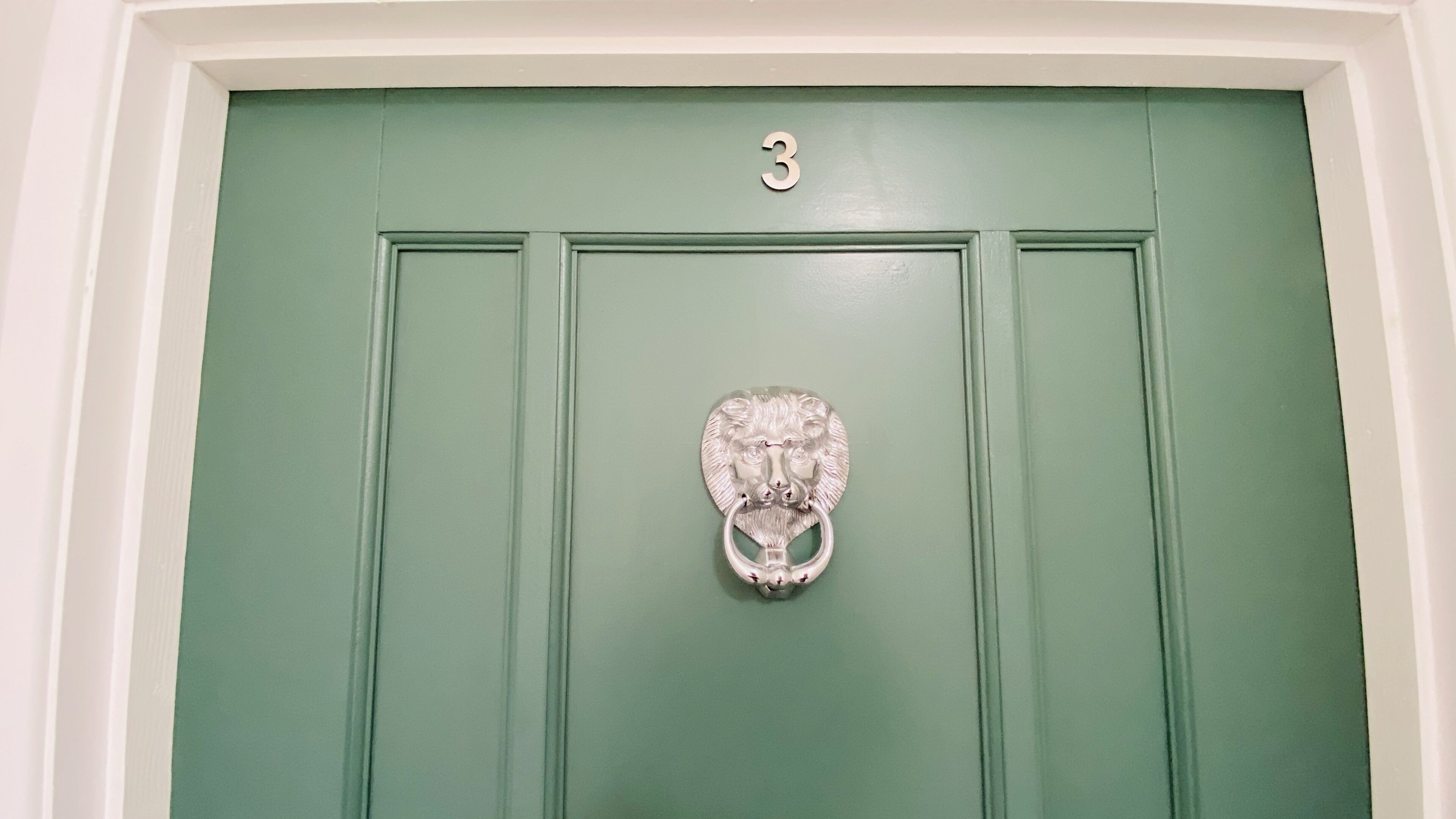 Une porte verte, avec le chiffre « 3 » au-dessus et une poignée de porte en argent en forme de tête de lion.