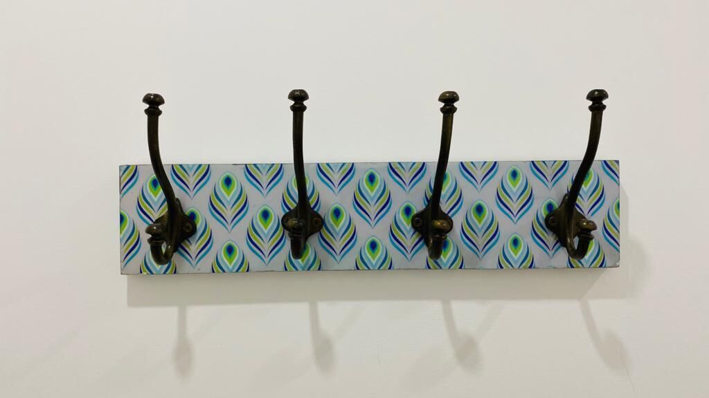A wall-mounted metal hookboard with four black hooks against a patterned tile background.