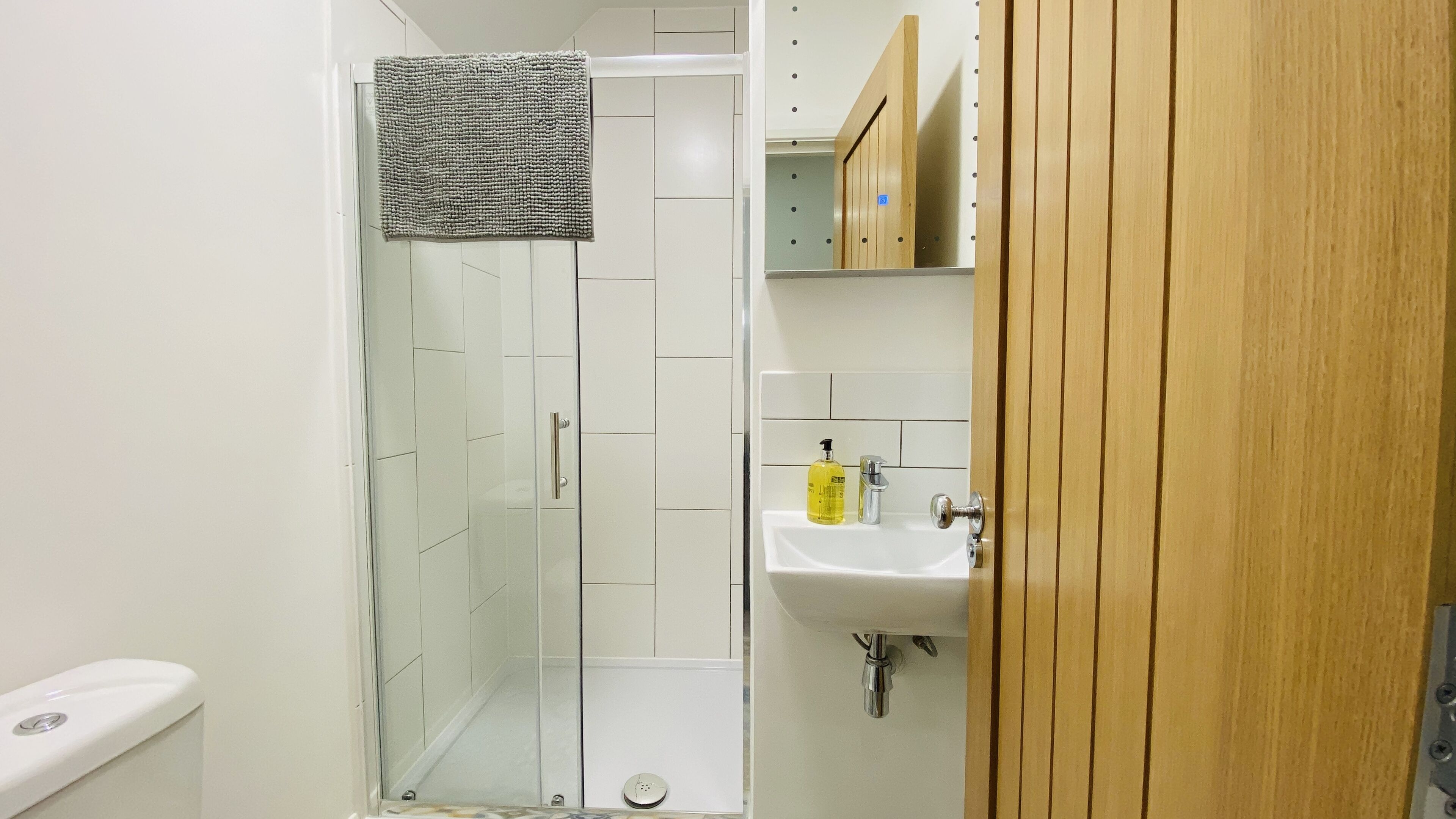A bathroom with a glass shower enclosure, a white sink with a mirror, and a wooden door.