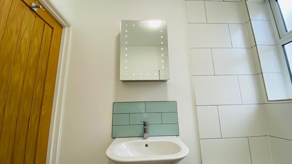 A bathroom with a sink, mirror, and green-tiled wall.