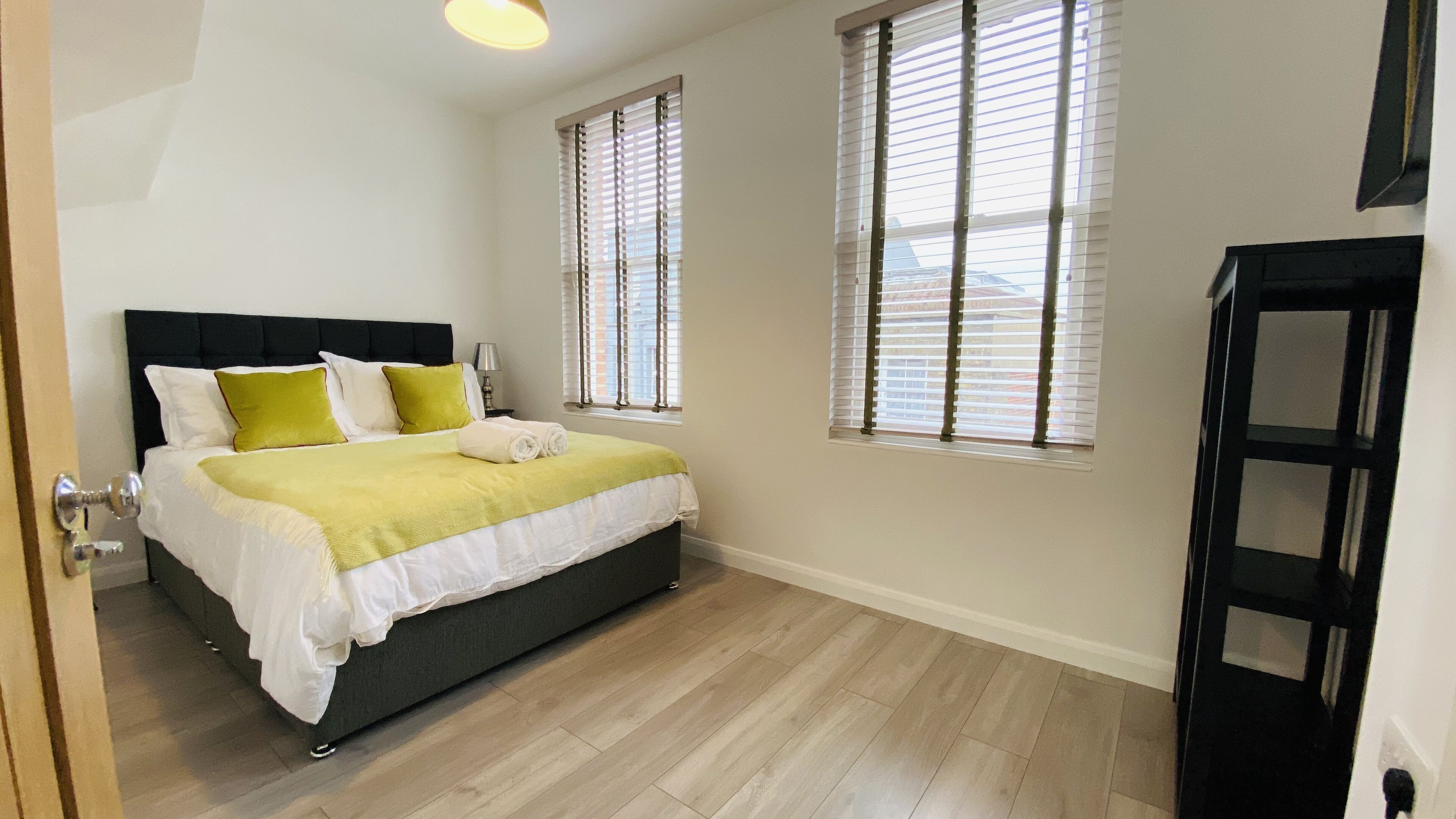 Un dormitorio con cama, dos ventanas, una mesita de noche y una puerta.