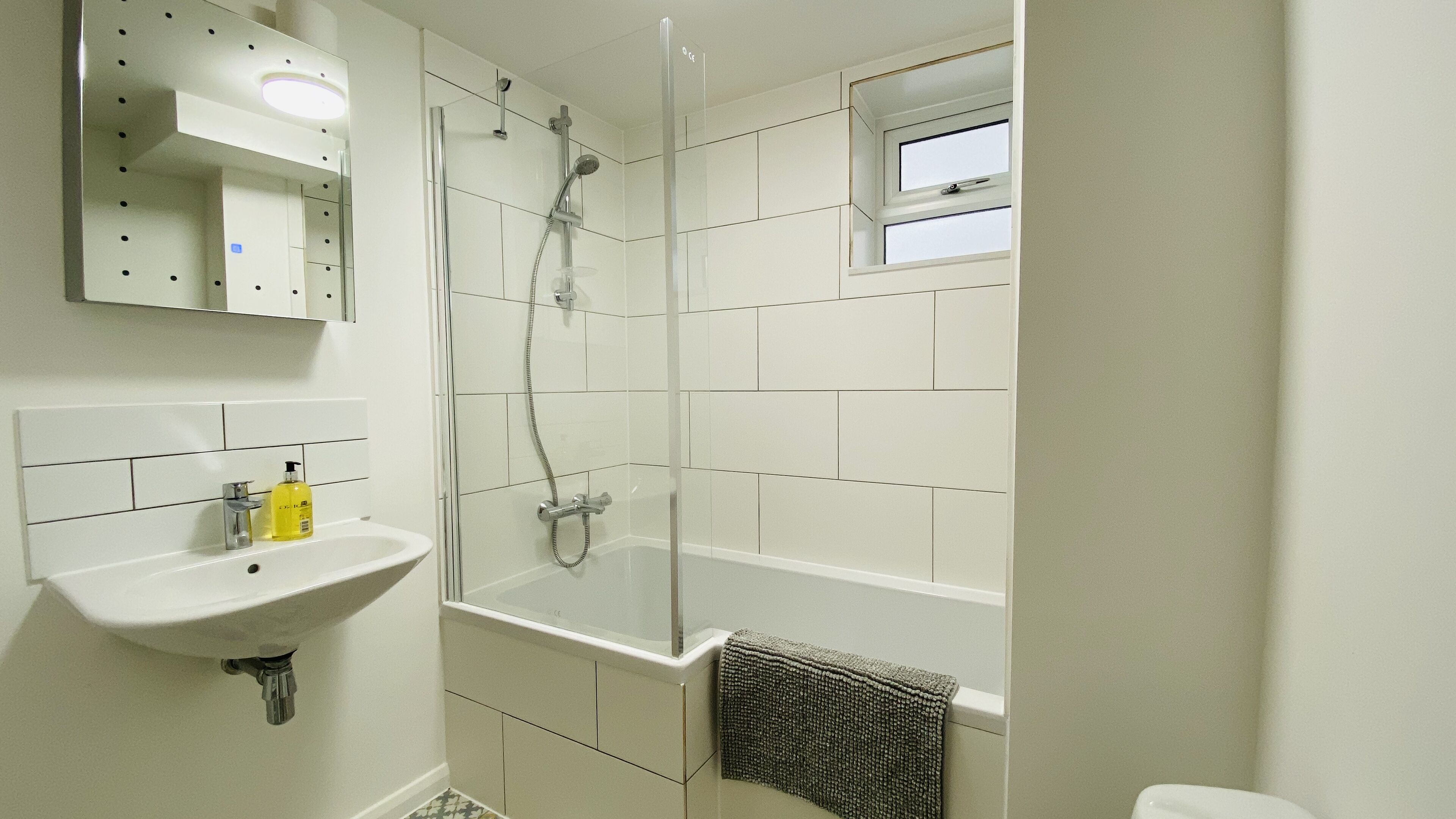 A bathroom with a glass-enclosed shower, a sink with a mirror above it, and a small window.