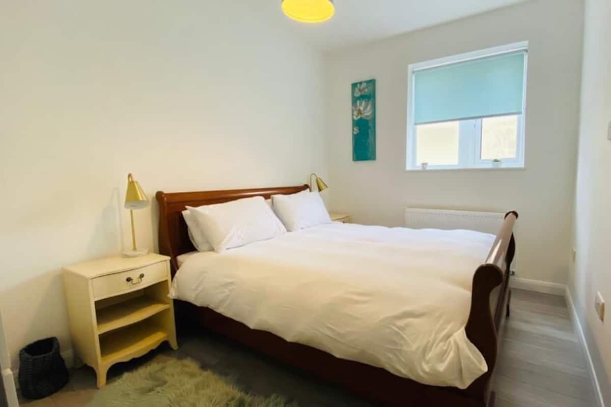 A bedroom with a single bed, a bedside table, a lamp, a window, and a radiator.