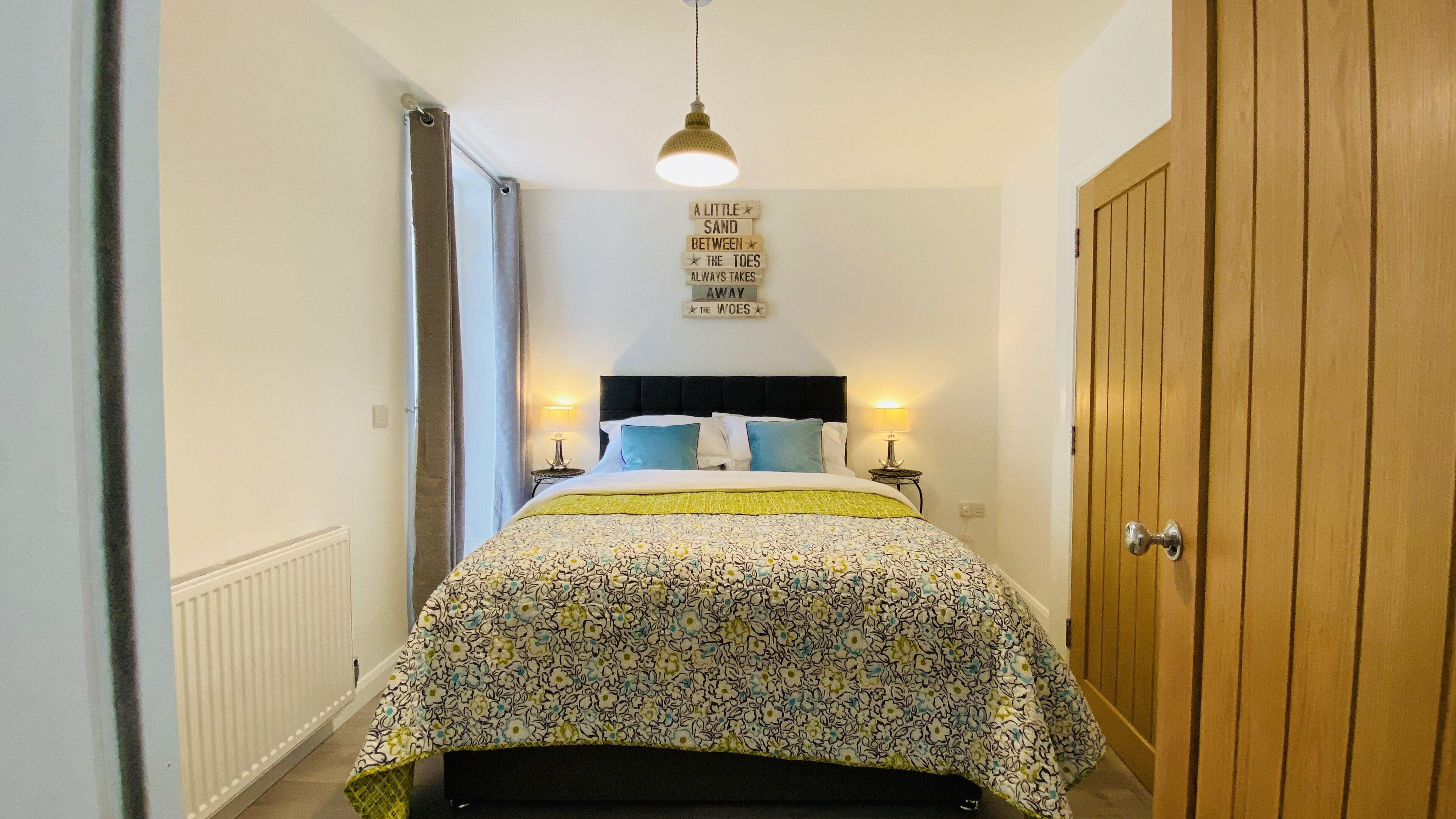 Een slaapkamer met een bed, nachtlampjes, een hanglamp, een houten kledingkast en een bord aan de muur.