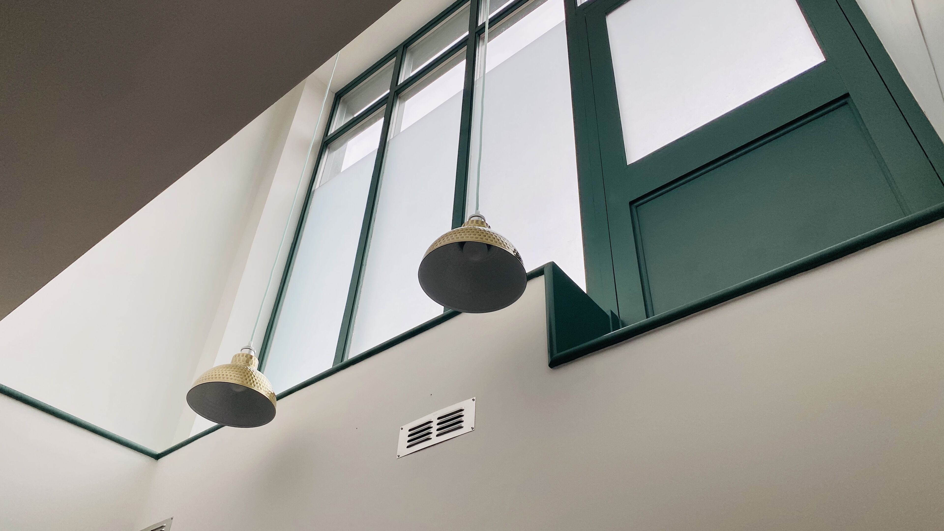 A room with a high ceiling, a window with green trim, and two hanging light fixtures.