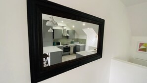 A modern kitchen with a dining area, a large mirror, and a staircase leading to an upper level.
