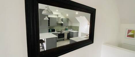 A modern kitchen with a dining area, a large mirror, and a staircase leading to an upper level.