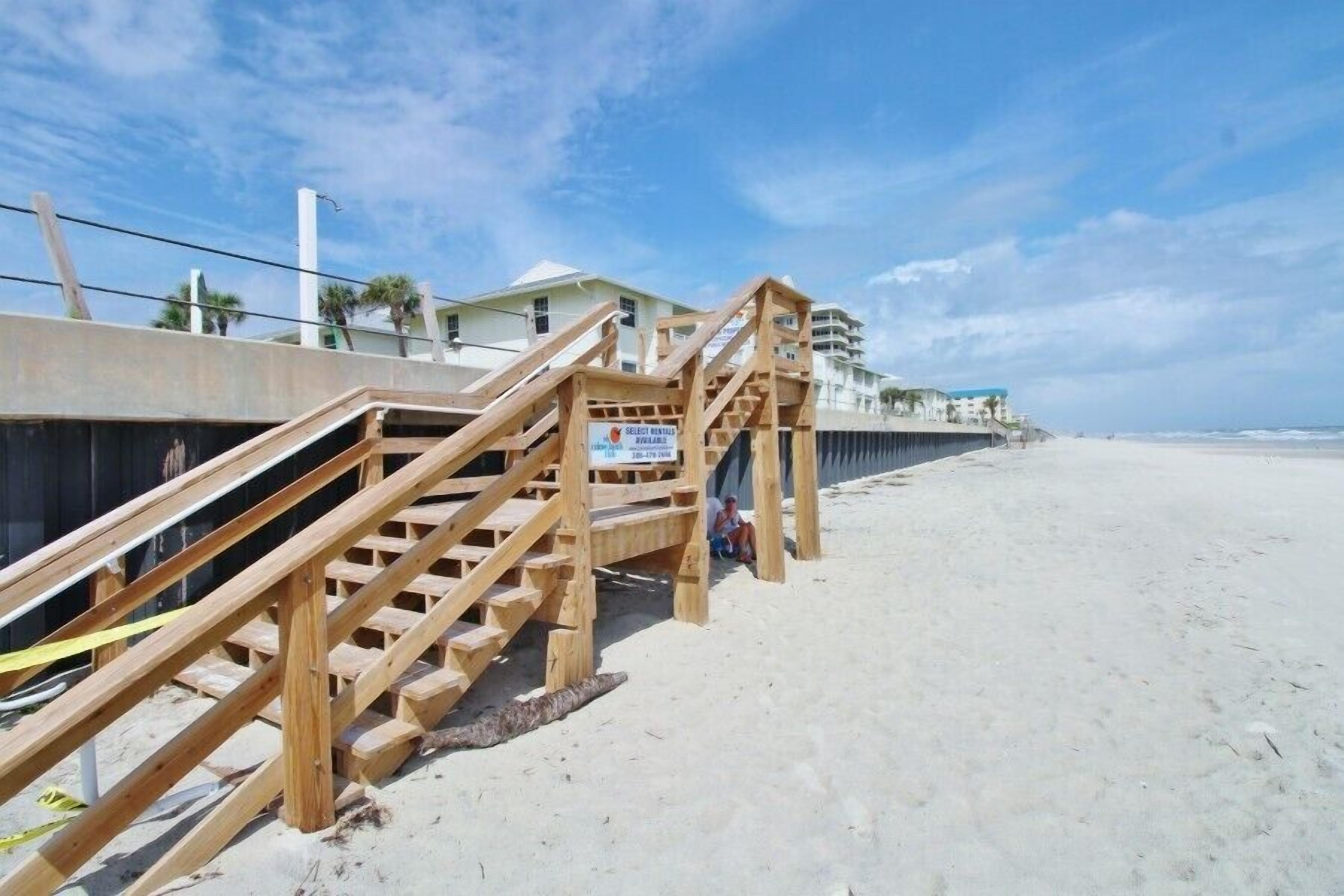 Eine Holztreppe führt zu einem Gebäude direkt am Strand, mit einem Schild, das einen Vermietservice für Strandliegen anzeigt.