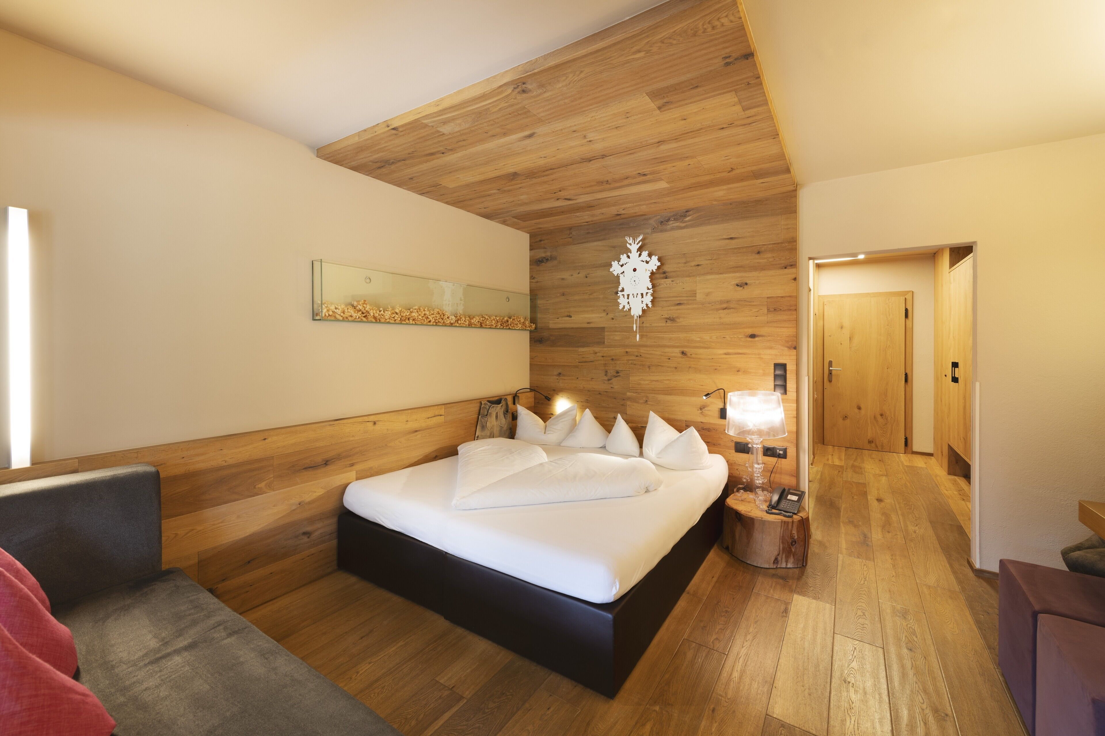 Ein modernes Schlafzimmer mit Holzbalkendecke, einem großen Bett mit weißer Bettwäsche, einem Nachttisch mit Lampe und einem Spiegel an der Wand.