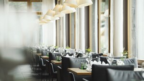 A restaurant with long tables, hanging lamps, and large windows. - Almhof Family Resort & SPA (Gerlos)