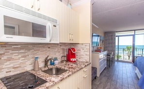 A modern kitchen with a microwave, sink, and coffee maker, and a balcony with a view.