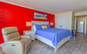 A bedroom with a bed, nightstands, a chair, a painting, and a door.